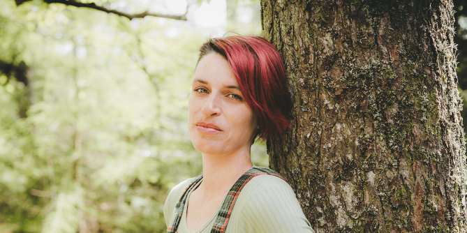 Kim Moore Poet standing next to a tree in the woods