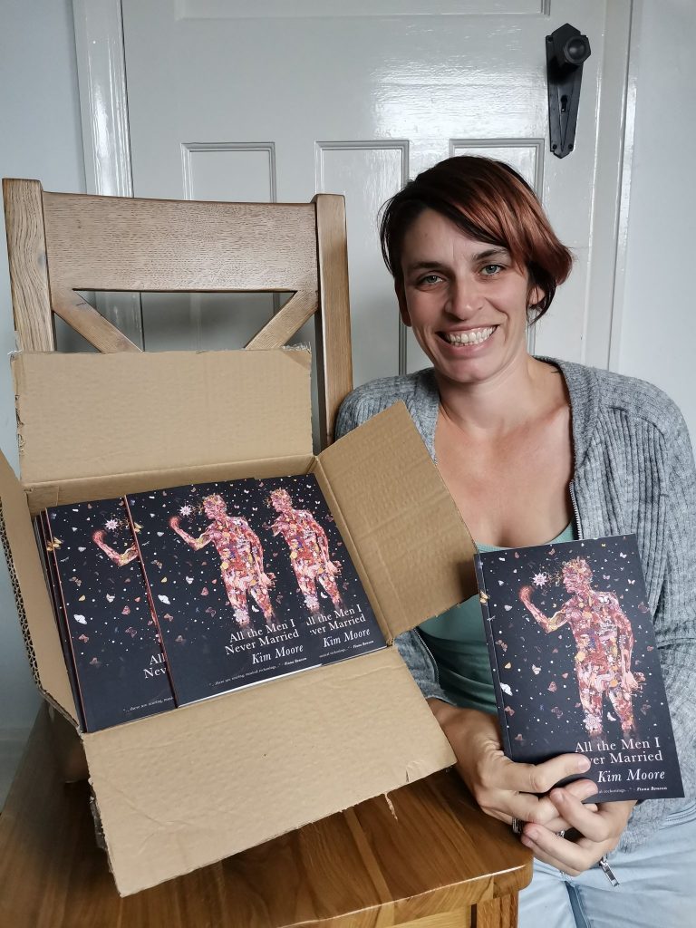 Kim Moore sitting next to a box containing copies of her second collection 'All The Men I Never Married' 